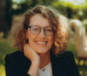 Profil de Solena Le Moigne, souriante, avec lunettes et cheveux blonds bouclés